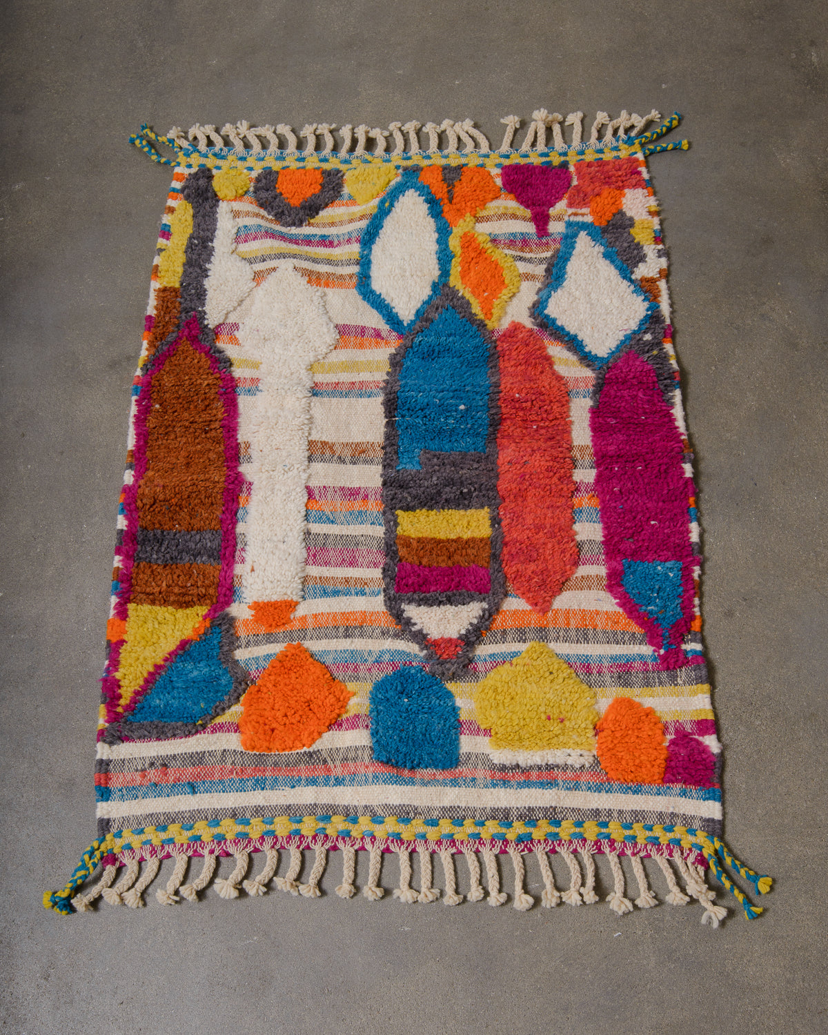 Small Berberlin Beniourain rug made of colourful wool with knotted and woven areas, laying on concrete floor.